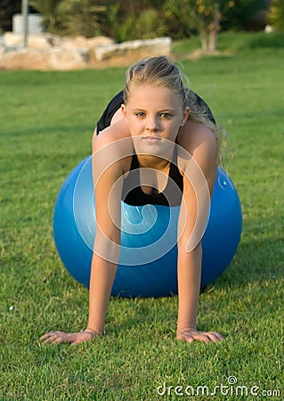 Young girl on blue fitness ball in the park