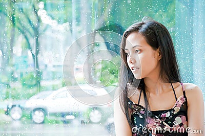 Young girl looking outside wet window