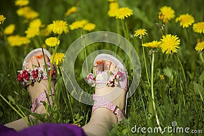 Young girl lying on grass in the middle of dandelions in sunlight with painted toe nails