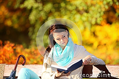 Young girl relaxing in autumnal park reading book