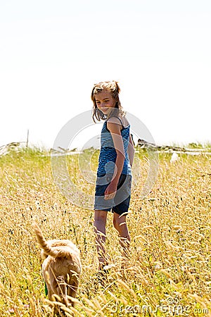 Young girl walking her dog through a field grass