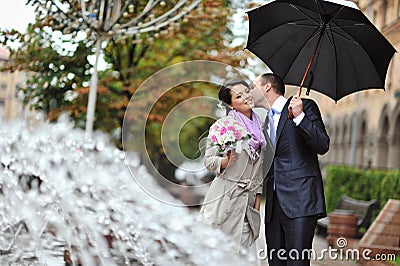 Young happy bride and groom kissing by the rain
