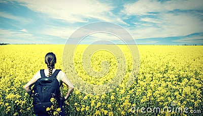 Young happy woman with backpack on a field of yellow rape