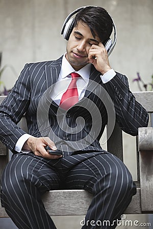 Young Indian businessman with eyes closed listening music on headphones