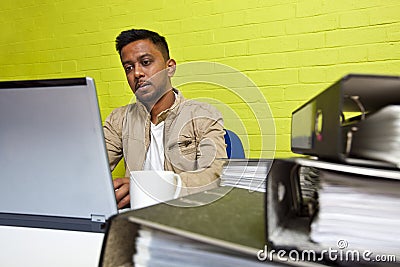 Young Indian man working at his computer surrounded by folders