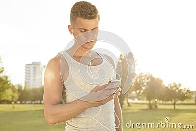 Young jogger listening to music through cell phone in park