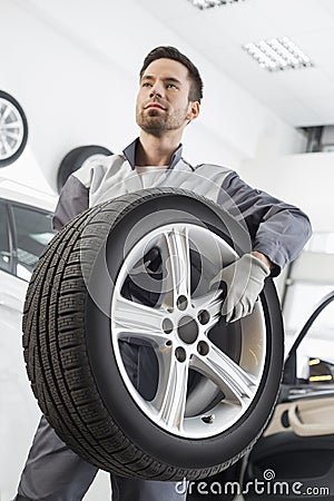 Young maintenance engineer carrying tire in automobile store