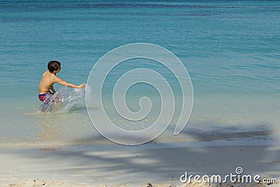 Young Male Child Splashing Water in the Ocean with Shadow of Palm Tree on Sandy Beach