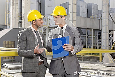 Young male engineers with clipboard discussing at construction site