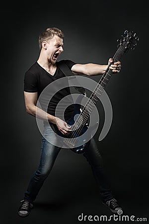 Young male musician playing a six-string bass guitar isolated