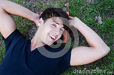 Young male student lying on grass with books