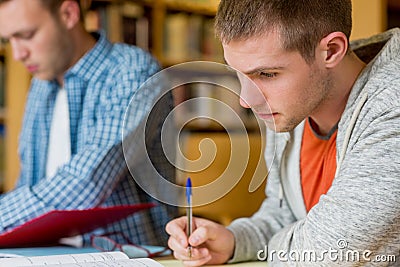 Young male students writing notes at library desk