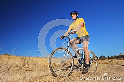 A young male with yellow shirt and helmet riding a bike outdoors