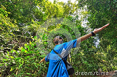 Young man arms raised enjoying the fresh air in green forest.