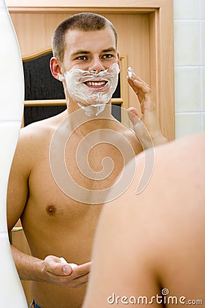 Young man in the bathroom s mirror with shave foam on face