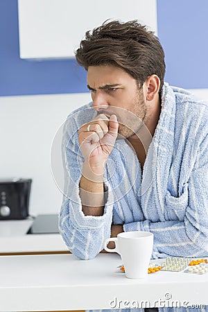 Young man coughing with coffee mug and medicine on kitchen counter