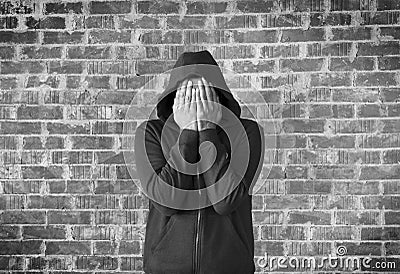 Young man covers his face with hands with bricks wall as background,black and white