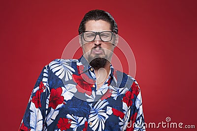 Young man in Hawaiian shirt making a face against red background