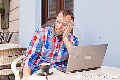 Young man with headache sitting in cafe with laptop and coffee.