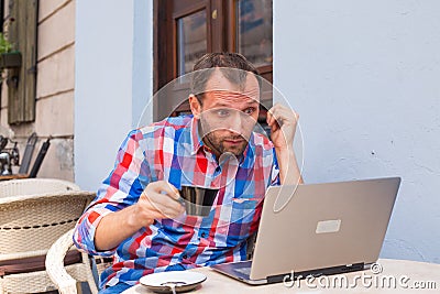 Young man with headache sitting in cafe with laptop and coffee.