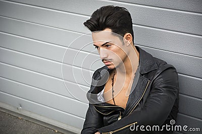 Young man with leather jacket looking away, sitting on the ground