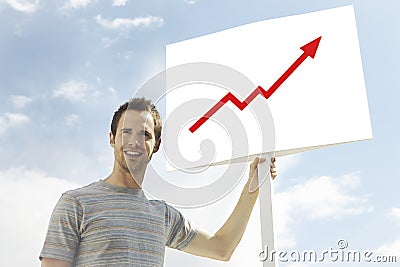 Young man looking away while holding arrow signboard against cloudy sky
