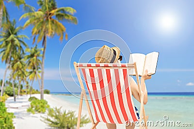 Young man lying on an outdoor chair and reading book, on a beach