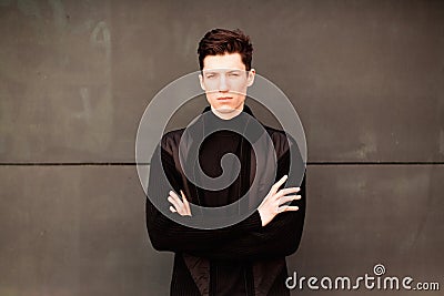 The young man model in a black jacket poses at a wall. image toned