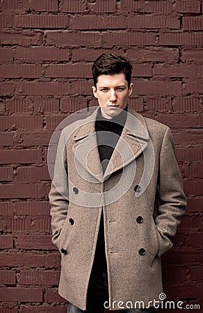 The young man model in a coat poses at a brick wall. Toned