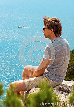 Young Man relaxing Outdoor on rocky cliff sitting and looking on Sea