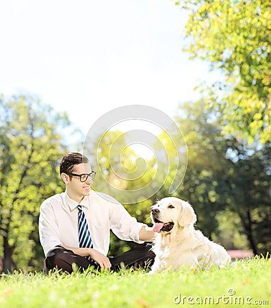 Young man sitting on grass next to a dog in a park on a sunny da