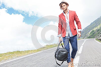 Young man strolls outside with bag