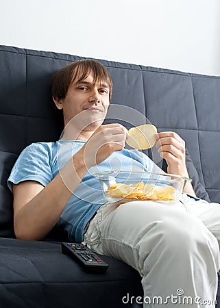 Young man watching tv and eating chips