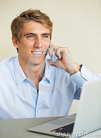 Young Man Working on Laptop Computer Talking on Phone