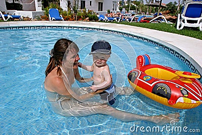 Young mother playing in children s swimming pool with toddler son and inflatable boat.