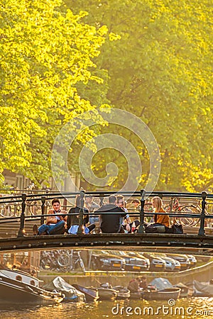 Young people relaxing on an Amsterdam canal bridge during sunset