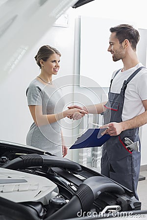 Young repair worker shaking hands with customer in car workshop