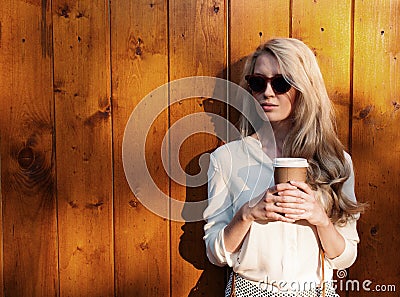 Young sexy blonde girl with long hair in sunglasses holding a cup of coffee have fun evening soft sunlight, warm, tonning