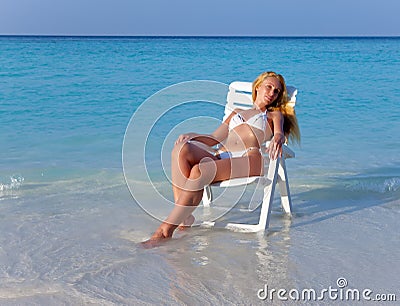 The young slender blonde in white sexual bikini a beach chair at ocean in a sunny day
