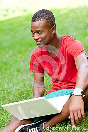 Young smiling african student sitting in grass with notebook
