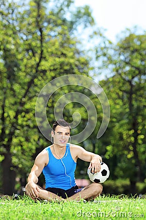 Young smiling male athlete sitting down on a grass with ball in