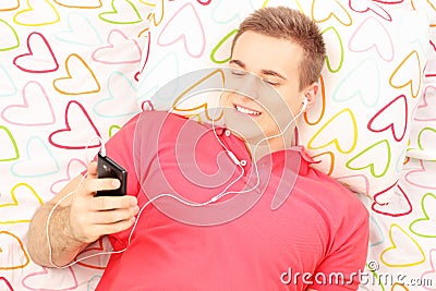 Young smiling man lying on a bed and listening music from his ph