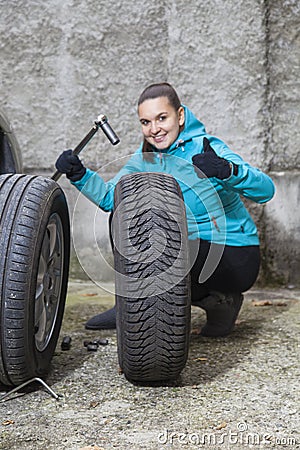 Young smiling woman driver replacing tires, showing OK sign