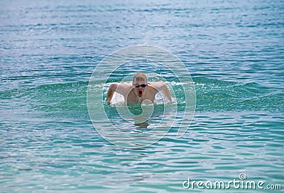 Young sporting man swims in sea butterfly stroke style