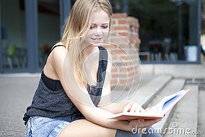 Young student outside reading book and smiling