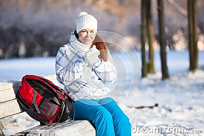 Young woman with backpack heating hands in mittens at winter, copyspace