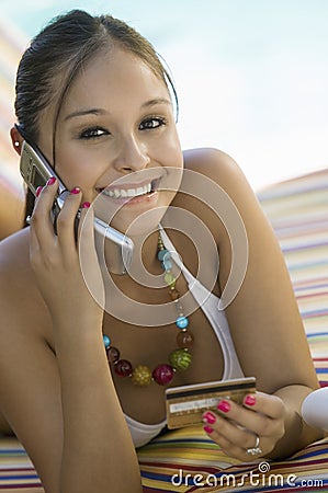 Young woman in bikini on deck chair by pool making credit card purchase on cell phone portrait