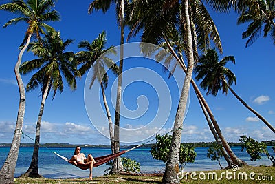 Young woman in bikini sitting in a hammock between palm trees, O