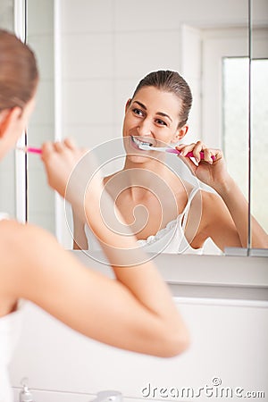 Young woman brushing her teeth in front of a mirro