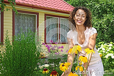 Young woman care of flowers in garden near house
